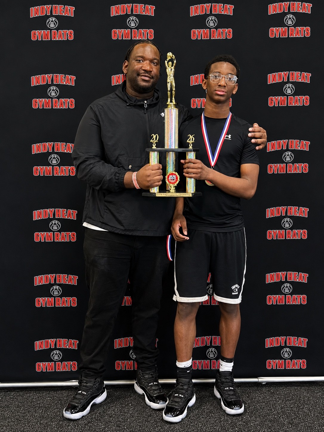 A Team Infinity athlete and an adult hold a basketball trophy together.