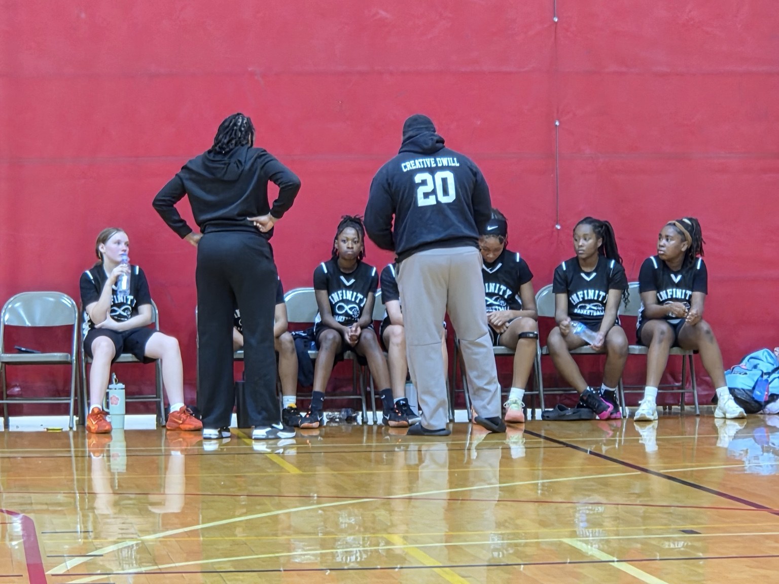 Team Infinity girls players listen to their coaches from the bench during a game.