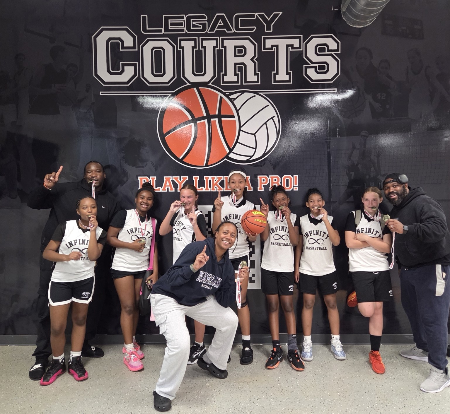Team Infinity girls players and coaches celebrate together with medals after a tournament.
